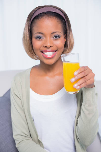 istock Pretty woman sitting on sofa holding orange juice 852218646