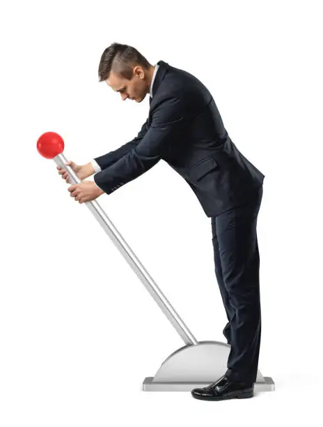 Photo of A businessman stands at a large lever with a red round knob and starts to move it.