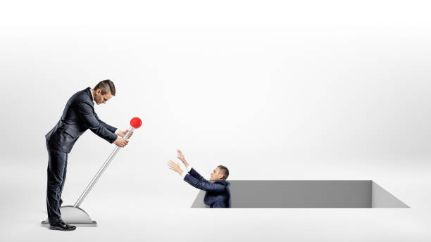 istock A businessman turns a large lever helping another man fallen inside a large square hole in the ground. 852221146