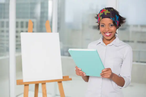 Smiling artistic woman holding sketchpad and looking at camera
