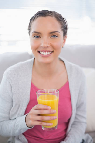 istock Smiling woman sitting on sofa and holding orange juice 852239694