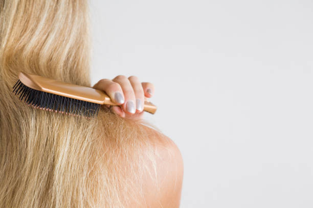 Woman's hand brushing blonde hair. Cares about a healthy and clean hair. Beauty salon. Empty place for a text on the gray background. Woman's hand brushing blonde hair. Cares about a healthy and clean hair. Beauty salon. Empty place for a text on the gray background. human hair women brushing beauty stock pictures, royalty-free photos & images