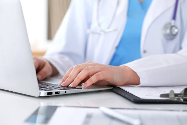 istock Close up of unknown female doctor typing on laptop computer while sitting  at the table 852271218