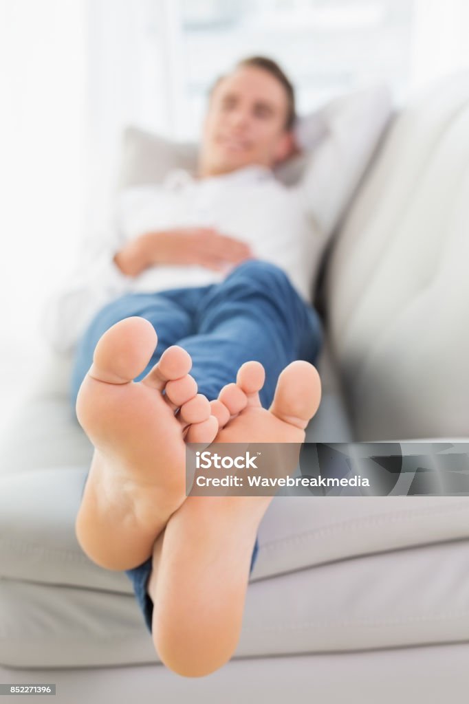 Full length of a relaxed young man lying on sofa Full length of a relaxed young man lying on sofa in a bright house 20-29 Years Stock Photo