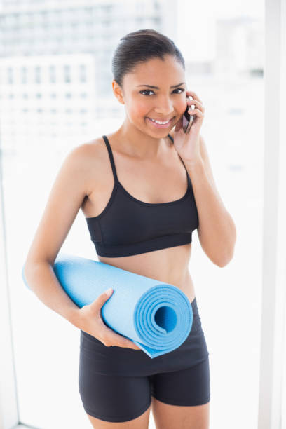 istock Fit dark haired model in sportswear carrying exercise mat and making a phone call 852285666