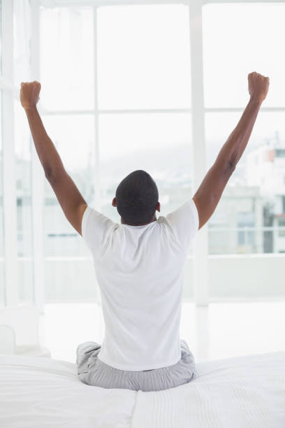 istock Afro man waking up in bed and stretching his arms 852288808