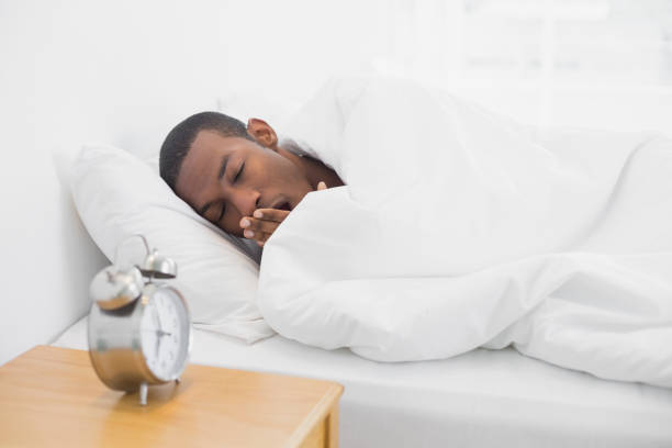 istock Afro man yawning in bed with alarm clock in foreground 852292872
