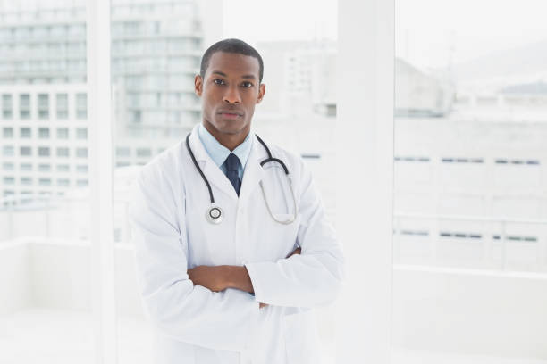 serious doctor with arms crossed in a medical office - serious african ethnicity mid adult bright imagens e fotografias de stock