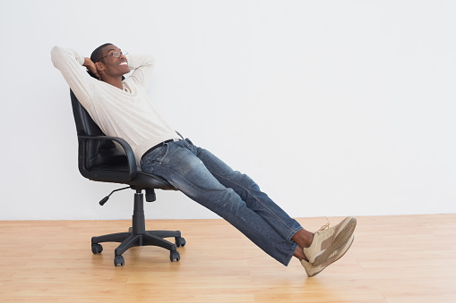 Thoughtful casual Afro young man sitting on office chair in an empty room