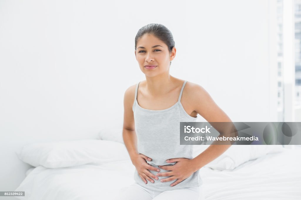 Lässige Frau mit Magenschmerzen im Bett sitzen - Lizenzfrei Hand am Bauch Stock-Foto