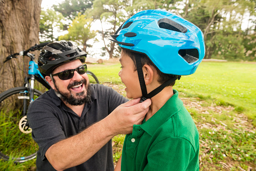 This is a royalty free, color photograph of a California Bay area father and mixed race son spending time together outdoors in the park. They wear bicycle helmets for safety as the boy is just learning how to ride a bike. Photographed with a Nikon D800 DSLR camera.