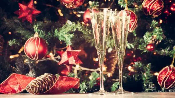Two glasses of champagne with Christmas tree background. Holiday season background. Traditional red and green Christmas decoration with lights. Holiday party. Horizontal, wide screen format