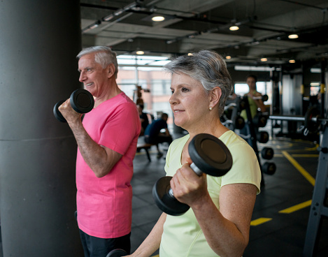 Portrait of two senior adults exercising at the gym lifting free weights - healthy lifestyle concepts
