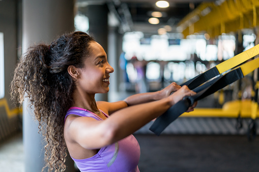 Happy Latin American woman suspension training at the gym â fitness concepts