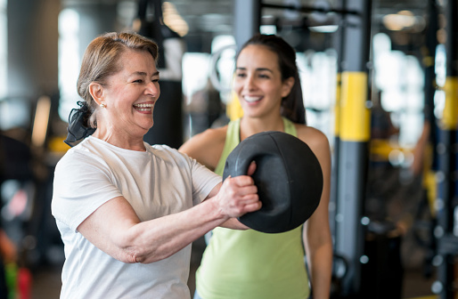 Adult woman exercising at the gym with a personal trainer and looking very happy - healthy lifestyle concepts