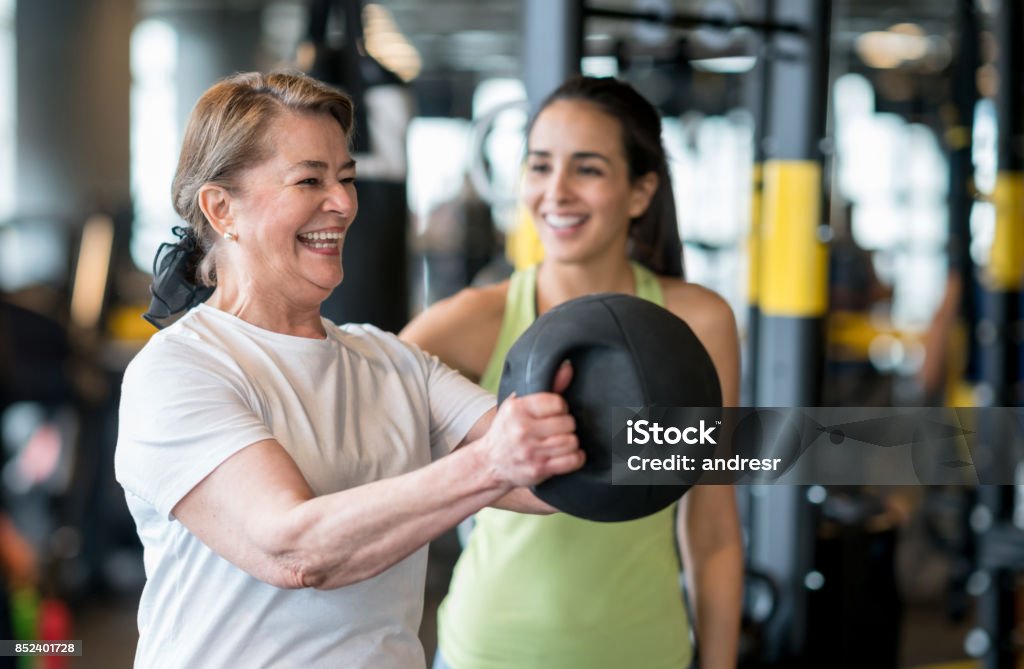 Adult woman exercising at the gym with a personal trainer Adult woman exercising at the gym with a personal trainer and looking very happy - healthy lifestyle concepts Fitness Instructor Stock Photo