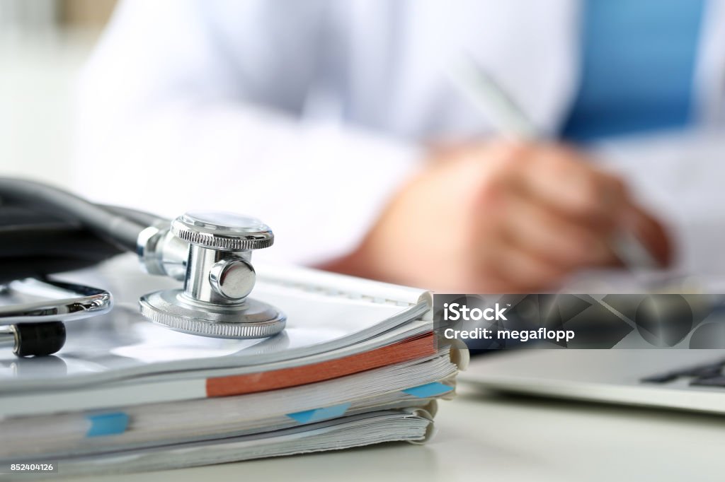 Stethoscope head lying on medical forms closeup Stethoscope head lying on medical forms on clipboard closeup while medicine doctor working in background. Patient history list, visit check, 911, medical calculation and statistics, healthy lifestyle concept Healthcare And Medicine Stock Photo
