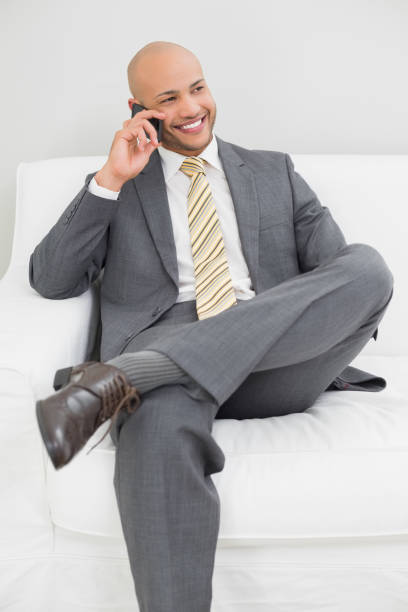 uomo d'affari che usa il cellulare sul divano di casa - well dressed front view looking at camera full length foto e immagini stock