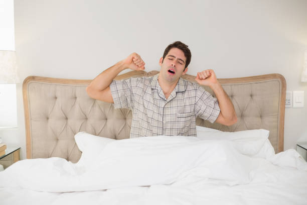 istock Young man waking up in bed and stretching his arms 852411044