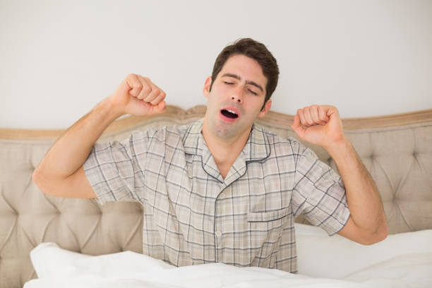 istock Young man waking up in bed and stretching his arms 852411056