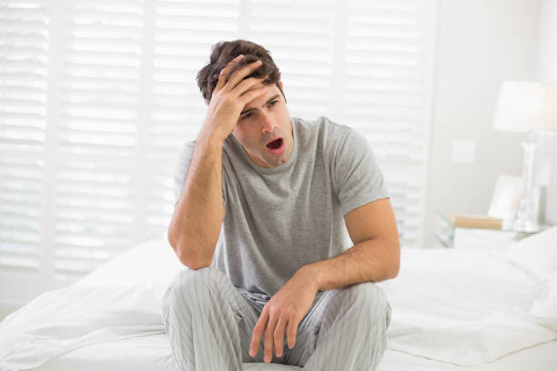 istock Sleepy young man sitting and yawning in bed 852412374