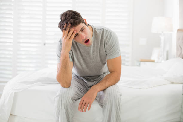 istock Sleepy young man sitting and yawning in bed 852412386