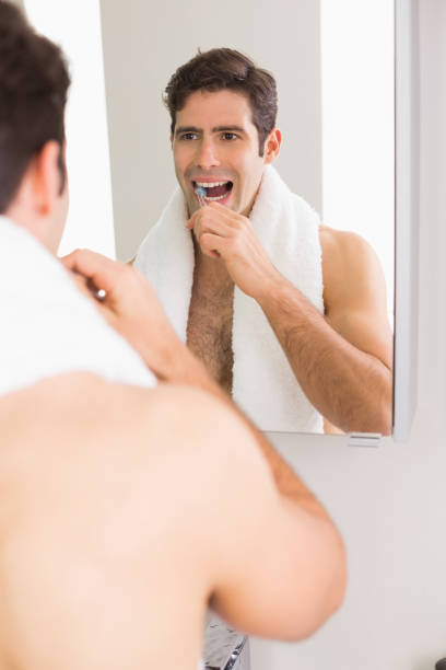 istock Young shirtless man with reflection brushing teeth 852419750