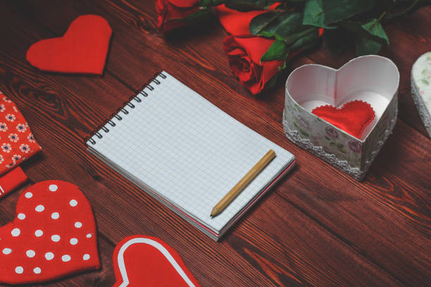 istock Opened mock up notepad, toy hearts and red roses on wooden table. Romantic 852470656