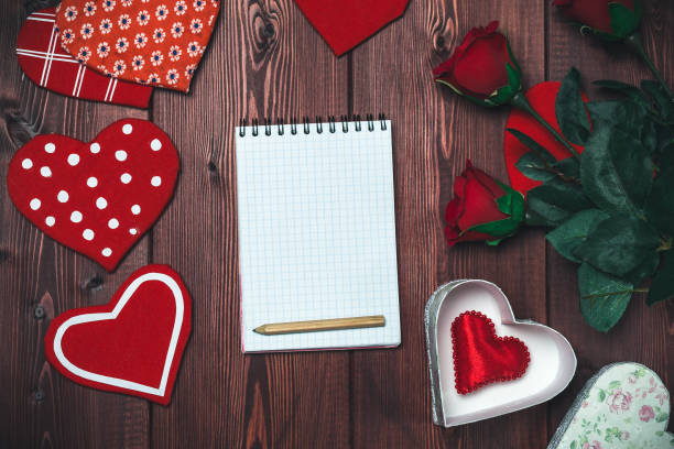 istock Opened mock up notepad, toy hearts and red roses on wooden table. Romantic 852470662