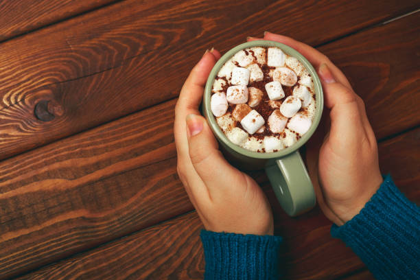 istock Female hands holding hot chocolate with marshmallow and cinnamon above rustic 852474114