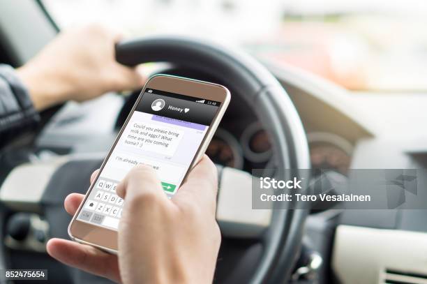 Texting While Driving Car Irresponsible Man Sending Sms And Using Smartphone Writing And Typing Message With Cellphone In Vehicle Holding Steering Wheel With Other Hand Stock Photo - Download Image Now