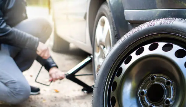 Driver changing spare tyre after accident. Broken and flat car wheel after crash.