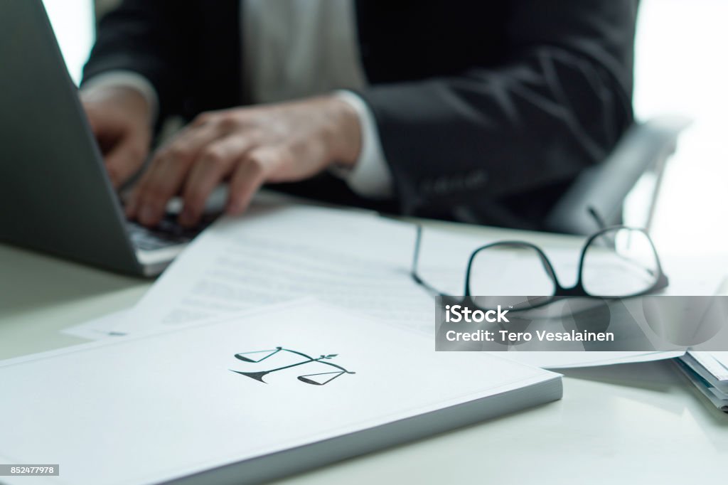 Abogado que trabajaba en la oficina. Abogado de la escritura de un documento legal con ordenador portátil. Gafas en la mesa. Pila de papel con el símbolo de la escala y la justicia. Concepto ley firme y de negocios. - Foto de stock de Abogado libre de derechos