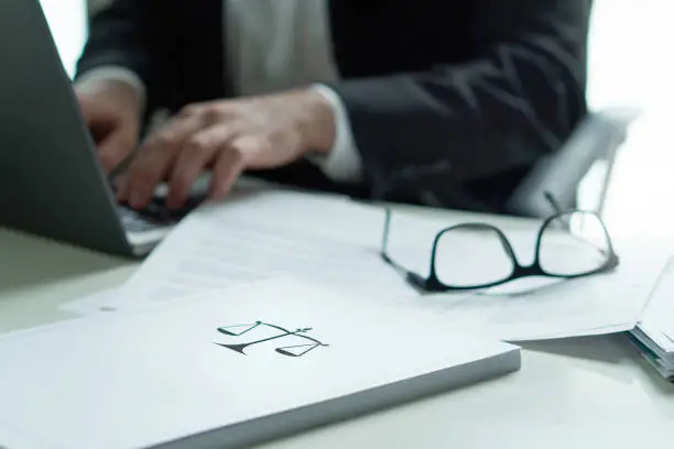 Lawyer working in office. Attorney writing a legal document with laptop computer. Glasses on table. Pile of paper with scale and justice symbol.