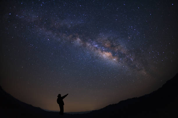 istock A Man is standing next to the milky way galaxy pointing on a bright star, Long exposure photograph, with grain. 852515744