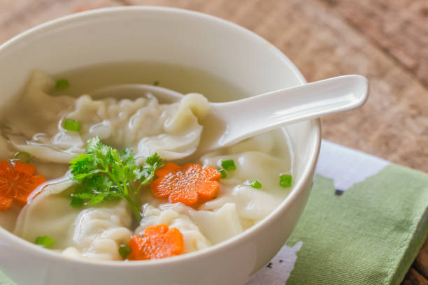 bouchent soupe wonton porc haché dans un bol blanc sur serviette mis sur la table en bois. maison wonton délicieux en soupe claire pour le petit déjeuner ou déjeuner ou dîner. soupe wonton est toujours populaire nourriture chinoise. - carrot close up silverware cutting board photos et images de collection