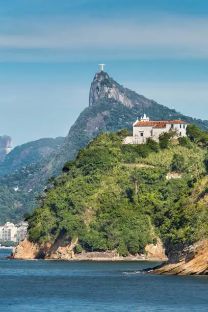 Christ the Redeemer viewed from Icarai Beach in Niteroi, with Guanabara Bay and the old Boa Viagem church surrounded by tropical trees on the foreground. Clear sunny day in Rio de Janeiro.