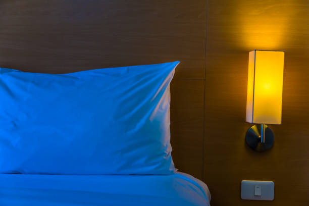 istock bedside lamp with its warm light turned on next to white bed and pillow at night with space for text or copy space, good for home at night or loneliness concept 852724700