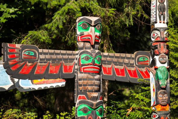 Native totem pole in BC Vancouver: Native American Indian totem pole in Stanley Park, Vancouver British Columbia. Totem poles are monumental carvings, a type of Northwest Coast art, consisting of poles, posts or pillars, carved with symbols or figures. They are usually made from large trees, mostly western red cedar, by indigenous peoples of the Pacific Northwest coast of North America pacific northwest totem poles stock pictures, royalty-free photos & images