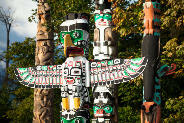 Native totem pole in BC Vancouver: Native American Indian totem pole in Stanley Park, Vancouver British Columbia. Totem poles are monumental carvings, a type of Northwest Coast art, consisting of poles, posts or pillars, carved with symbols or figures. They are usually made from large trees, mostly western red cedar, by indigenous peoples of the Pacific Northwest coast of North America pacific northwest totem poles stock pictures, royalty-free photos & images