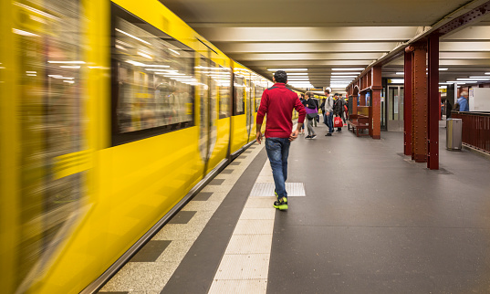 Berlin, Gernany - September 12, 2017: One commuter is walking towards a moving train while other waiting commuter are in the background, at the Metro station Alexander platz in Berlin. The U-bahn serves 170 stations spread across ten lines with a total track length over 150 km