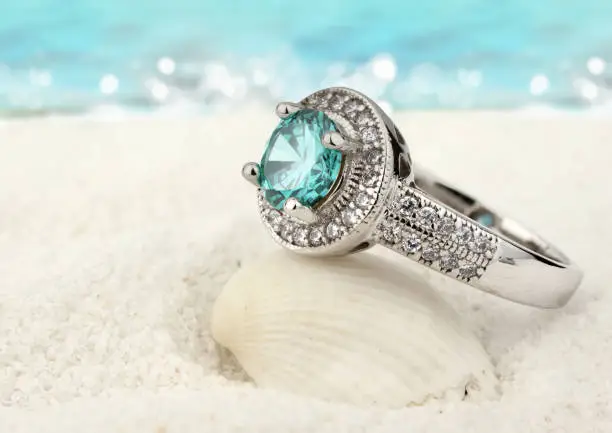 Jewelry ring with aquamarine gem on sand beach background