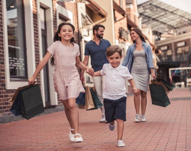 Family doing shopping Beautiful parents and their cute little kids are carrying shopping bags, holding hands and smiling while walking down the street mall walker stock pictures, royalty-free photos & images