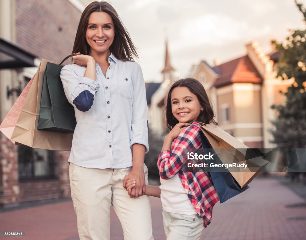 Mom and daughter Beautiful mom and her cute little daughter are carrying shopping bags, holding hands, looking at camera and smiling while standing outdoors Mother Stock Photo