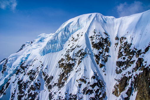 Packed Snow Capped Craggy Sheer Mountain Peak.  Aerial View of the Great Alaskan Wilderness, Denali National Park, Alaska.  A Beautiful Snowscape of Rock, Snow, and Ice.