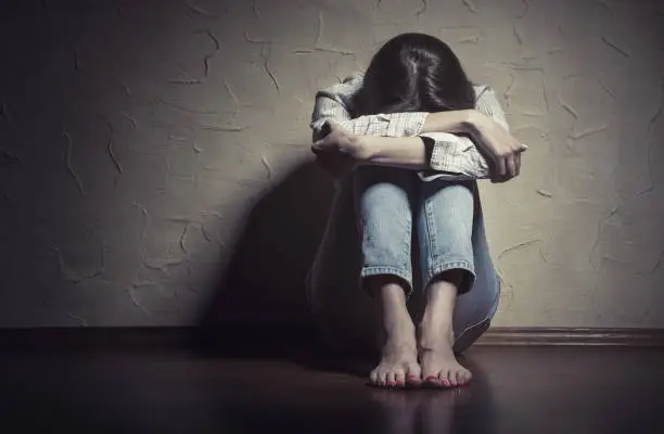 Young sad woman sitting alone on the floor in an empty room