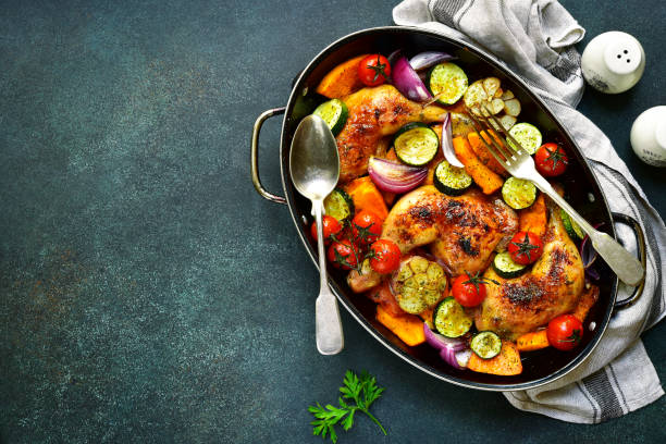 Chicken legs roasted with vegetables in a skillet pan Chicken legs roasted with vegetables in a skillet pan over dark slate,stone or concrete background.Top view. paleo diet photos stock pictures, royalty-free photos & images