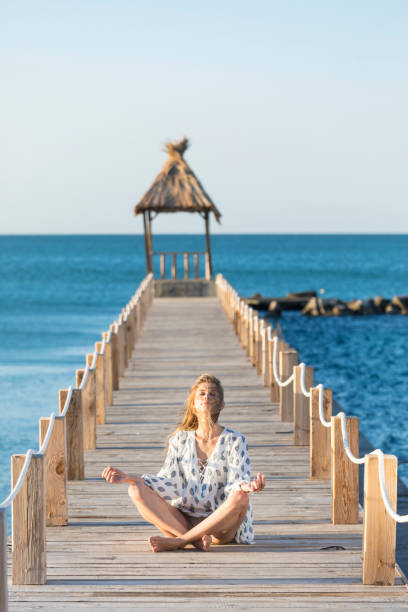 istock Young woman sitting on pier and practicing 852940176