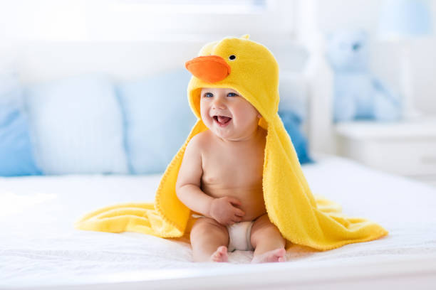 Cute baby after bath in yellow duck towel Happy laughing baby wearing yellow hooded duck towel sitting on parents bed after bath or shower. Clean dry child in bedroom. Bathing and washing of little kids. Children hygiene. Textile for infants. baby boys stock pictures, royalty-free photos & images