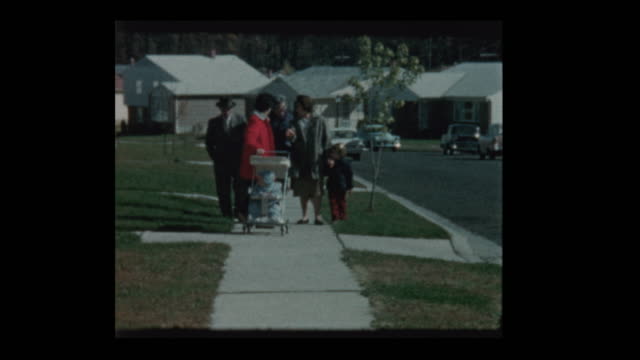 1960's Family takes baby for walk in antique stroller on suburban street